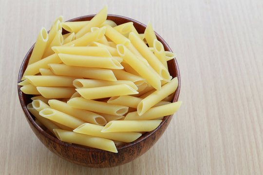 Raw Macaroni in the wooden bowl on wood background.