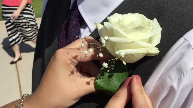 Woman pinning white corsage onto best man's tuxedo vest at wedding