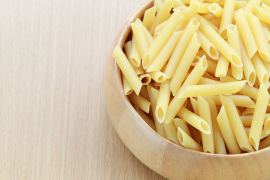 Raw Macaroni in the wooden bowl on wood background.