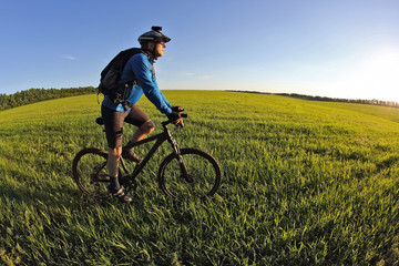 cyclist rides a bicycle on the green field towards the sun