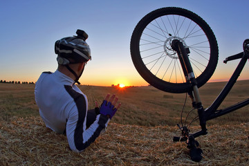 resting cyclist with a Bicycle looks at sunset.