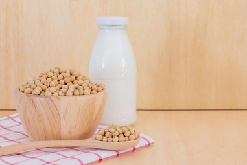 soy milk in glass bottle with soy beans in spoon on wooden background, Top view with copy space and text.
