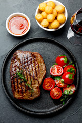 Grilled beef steak served on cast iron plate with tomato salad, potatoes balls and red wine. Barbecue, bbq meat beef tenderloin. Top view, slate background
