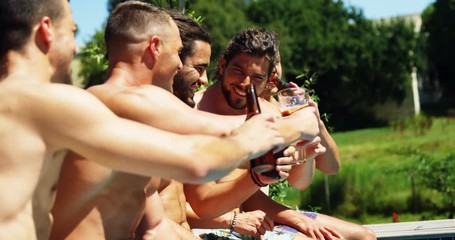 Group of friends toasting drinks while sitting on the edge of pool 