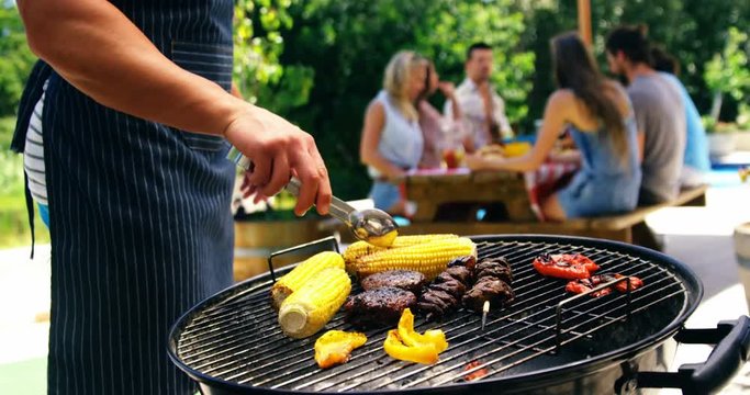 Mid section of man grilling corn, meat and vegetable on barbecue