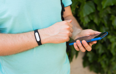 Close up of men's hand with a activity tracker and smart phone outdoors
