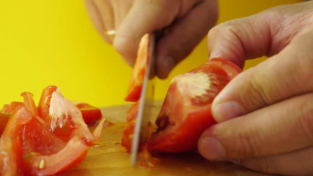 Cutting up ripe tomato with kitchen knife on wooden board on yellow background