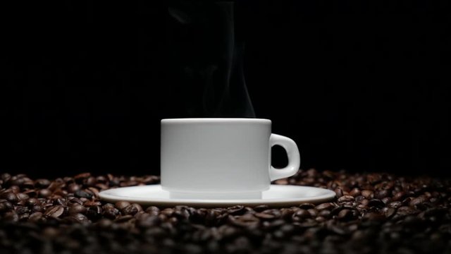 coffe cup and coffe beans. A white cup of evaporating coffee on the table with roasted bean. A cup with coffe bean as background 4k