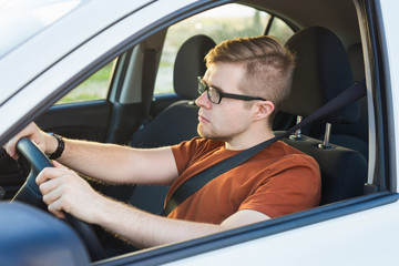 Handsome serious young man drives a car