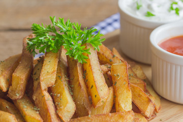 Homemade french fries serve with ketchup and sour cream or mayonnaise. Golden brown crispy french fries sprinkle with salt and oregano on wood plate for snack or appetizer. French fries on wood table.