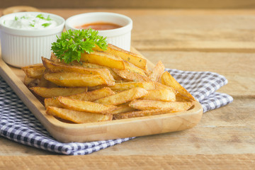 Homemade french fries serve with ketchup and sour cream or mayonnaise. Golden brown crispy french fries sprinkle with salt and oregano on wood plate for snack or appetizer. French fries on wood table.