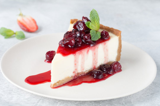 Slice of new york cheesecake with cherry sauce and mint leaf on top.