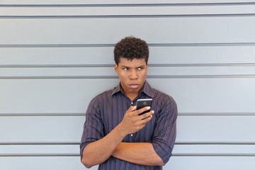 Young attractive man holding cell phone while standing alone and looking aware with serious angry face