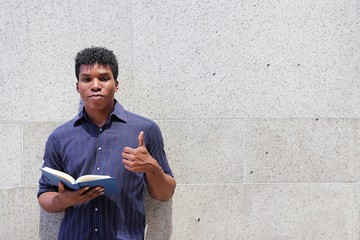 Attractive african american student holding book while standing against a gray concrete wall 