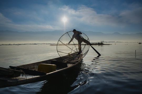 Burmese fisherman on bamboo boat catching fish in traditional way with handmade net.