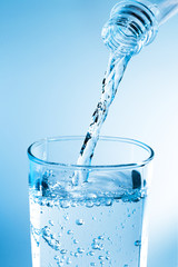 Pouring water from bottle into glass with blue light
