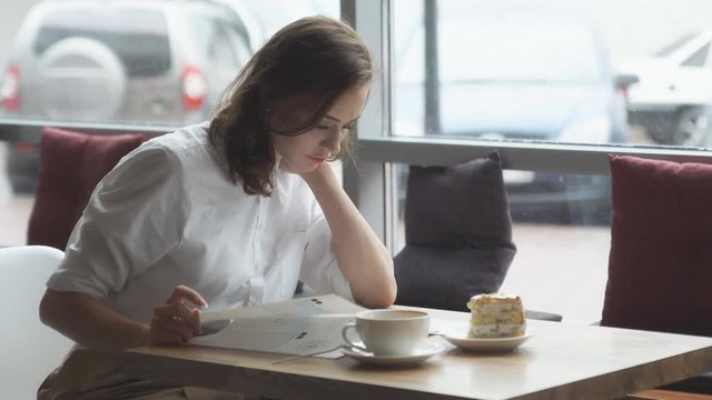 young business woman is resting during a lunch break at a cafe and leafing through women's fashion magazine