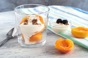 Dessert with peaches and cream . Peach in a glass with nuts and cream on a white wooden table.