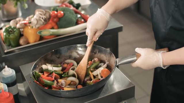 close-up chef actively working in the kitchen of an Asian restaurant mixed colorful vegetables are roasted in a wok in slow motion