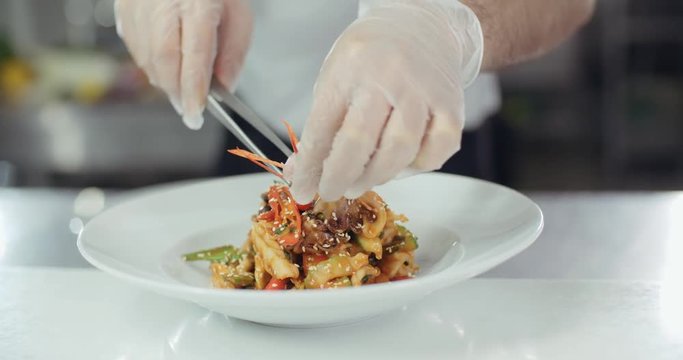 chef serves a dish of seafood on a plate adding the final ingredients