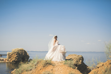 Fototapeta na wymiar Lovely bride in white wedding dress posing near the sea with beautiful background