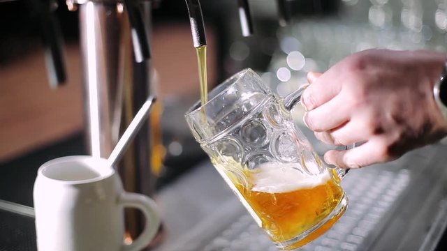 Pub, barman pours a light beer into a glass. 
