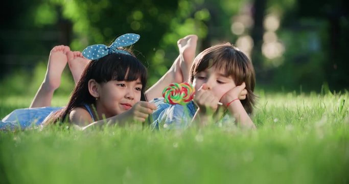 two little children with a Lollipop,Caucasian boy and Asian girl having fun lying on the grass in the Park