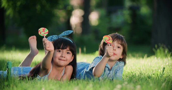 two little children with a Lollipop,Caucasian boy and Asian girl having fun lying on the grass in the Park