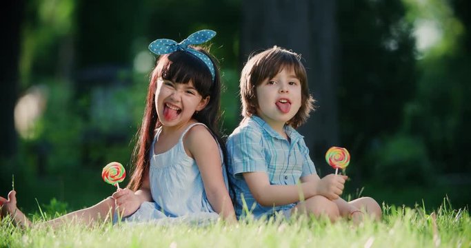 two small children,Caucasian boy and Asian girl having fun in the Park with a Lollipop