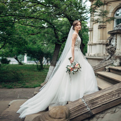 Bride in rich dress stands on the footsteps outside