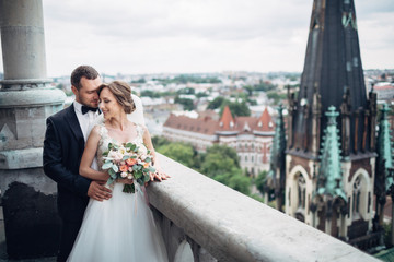 Classy wedding couple hugs on the roof of Gothic cathedral