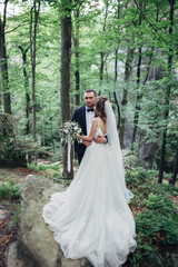 Wedding couple kises under the veil standing in the forest