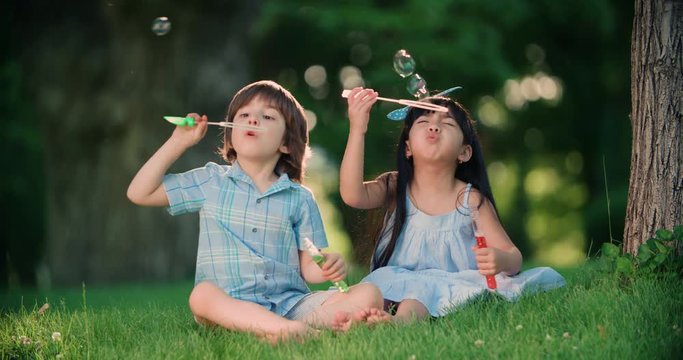 Happy children Caucasian boy and Asian girl blowing soap bubbles in spring Park, slow motion