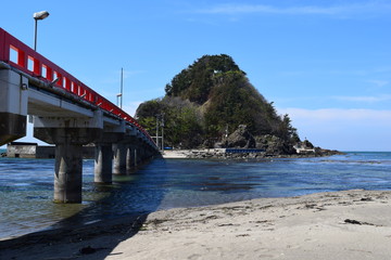 Fototapeta na wymiar 白山島（東北の江ノ島）／ 山形県鶴岡市の由良海岸沖にある白山島は、「日本の渚百選」と、「快水浴場百選」に選ばれた由良海岸のシンボル的な島で、その景観から「東北の江ノ島」と呼ばれています。由良海岸から島までは赤い白山橋が架けられており、歩いて島に渡ることが出来ます。