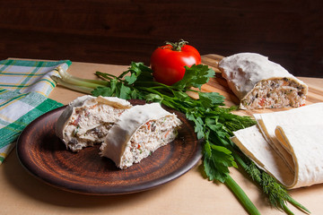 Two pieces of pita bread or lavash roll with cottage cheese or curd, chicken, tomatoes and herbs - dill, onion, parsley on brown clay plate..