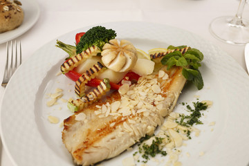 Hake fillet with grilled vegetables arranged on a plate, Traditional dish in elegant setting, Selective focus with soft light
