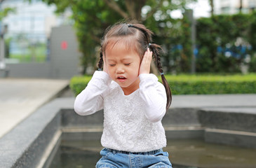 Child girl shutting down her ears, holding her hands to cover ears not to hear.