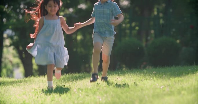 two kids,a boy and a girl running around in the garden holding hands and laughing ,slow motion