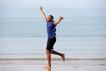 Full body excited african guy running on beach with arms raised