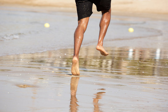 Young man running barefoot on beach