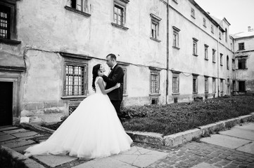 Amazing young attractive newly married couple walking and posing in the downtown with beautiful and ancient architecture on the background on their wedding day. Black and white photo.