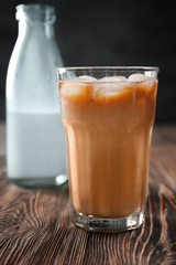 Glass with cold brew coffee and bottle of milk on wooden table