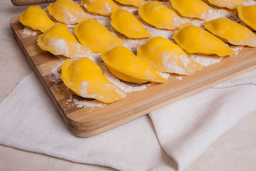 Ready for boiling vareniki, dumplings, pierogi on wooden cutting board with flour and wooden rolling pin, sieve ..