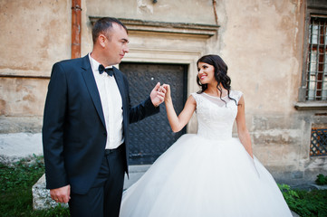 Fototapeta premium Amazing young attractive newly married couple walking and posing in the downtown with beautiful and ancient architecture on the background on their wedding day.