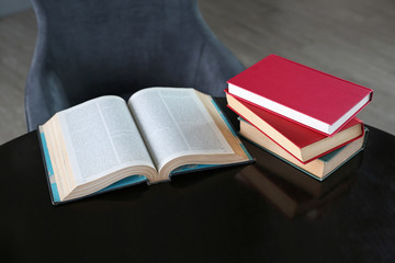 Open book and stack of hardcover books on wooden table.