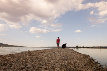 Fototapeta na wymiar Man and his dog walking on the sandy path across the lake on a beautiful summer sunset