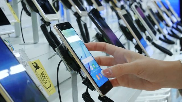 Customer chooses smartphone in electronics store. Gadget showroom at electronics store, buyers testing smartphones