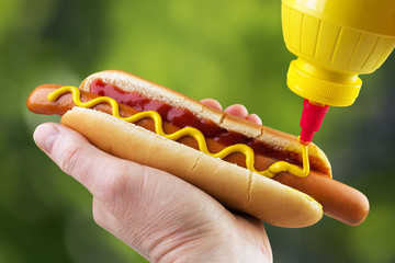 Adding yellow mustard to hot dog in hand