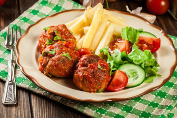 Roasted meatballs in tomato sauce with french fries and salad
