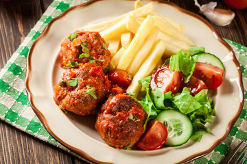 Roasted meatballs in tomato sauce with french fries and salad